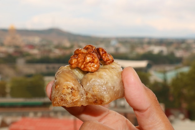 Closeup mano sosteniendo un pastel de baklava de nuez con vista borrosa de la ciudad en el telón de fondo