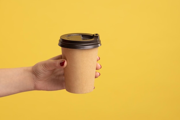 Closeup mão dando café em copo descartável bebida quente com cafeína para aumentar a energia na pausa para o café da manhã no trabalho bebida saborosa e relaxamento Estúdio interior isolado em fundo amarelo