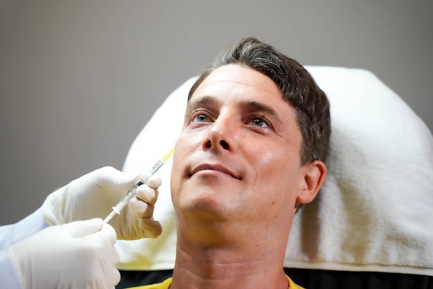 Closeup mãos de cosmetologista segurando uma seringa injetando soro no rosto do cliente