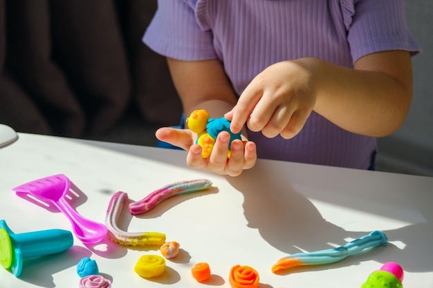 Closeup mãos de crianças com tartaruga de plasticina na mesa branca em casa jogos de desenvolvimento de habilidades motoras das crianças crianças com plasticina