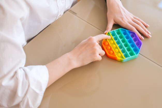 Foto closeup mãos de uma jovem irreconhecível brincando com um brinquedo de arco-íris, sentado à mesa