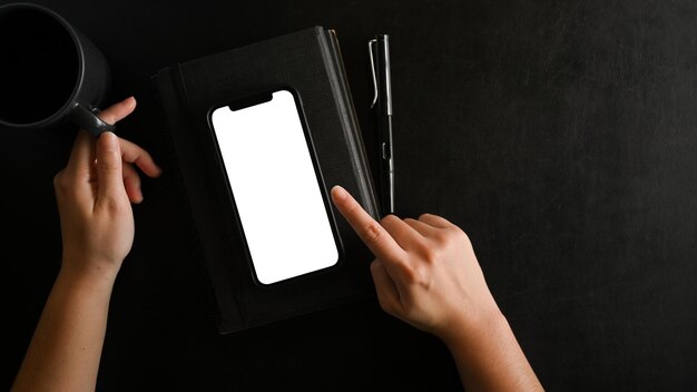 Closeup mãos femininas usando maquete de tela em branco de smartphone em plano de fundo preto vista superior