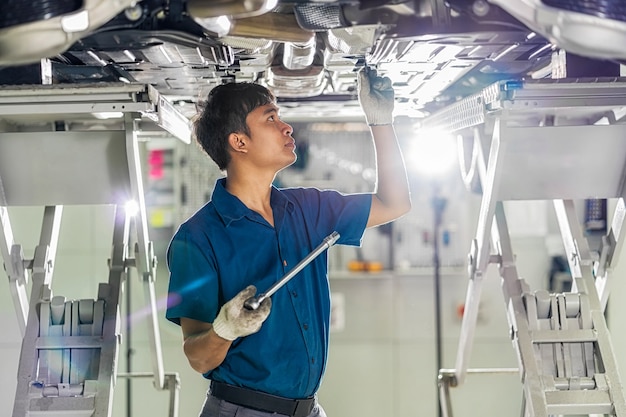 Closeup mecânico asiático reparando a mão embaixo do carro no centro de serviços de manutenção