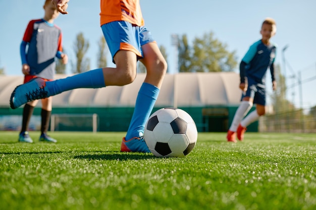 Closeup menino chutando bola enquanto jogava futebol com companheiros de equipe no campo de grama ao ar livre. Torneio de futebol para crianças