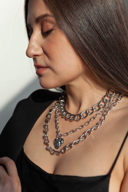 Closeup muchas cadenas de plata modernas con colgante en forma de corazón en morena modelo caucásico con pelo largo, collar de metal, luz del sol