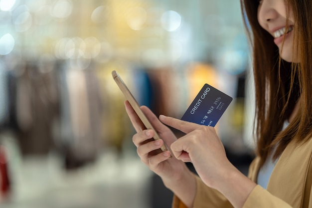 Closeup mujer asiática con tarjeta de crédito con móvil para compras en línea en grandes almacenes