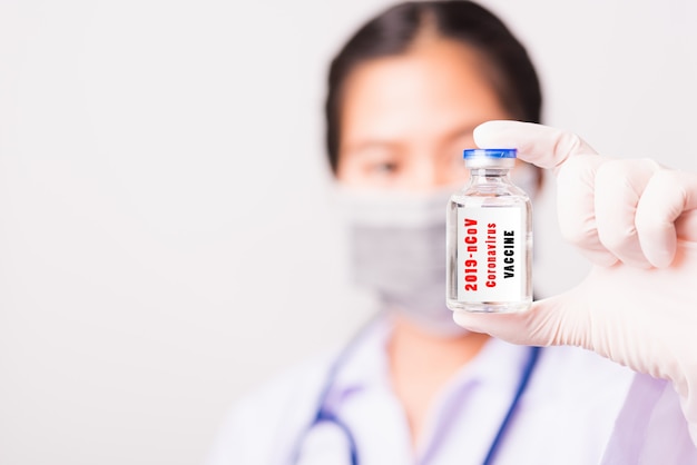 Closeup mujer doctora en uniforme con mascarilla protectora en laboratorio uso dedo sostenga vial botella de vacuna