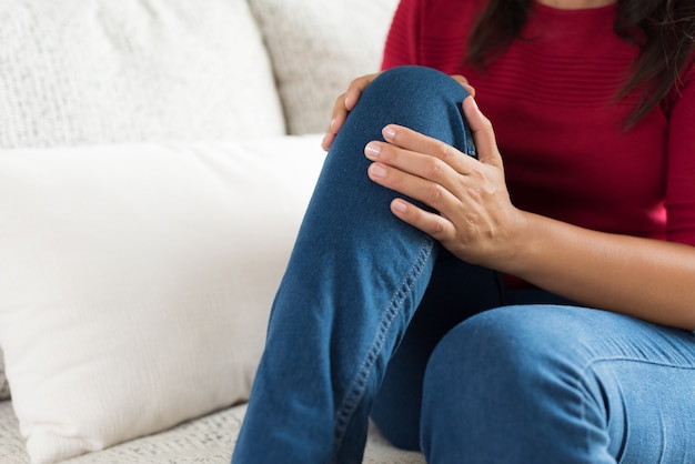 Closeup mujer joven sentada en el sofá y sintiendo dolor de rodilla