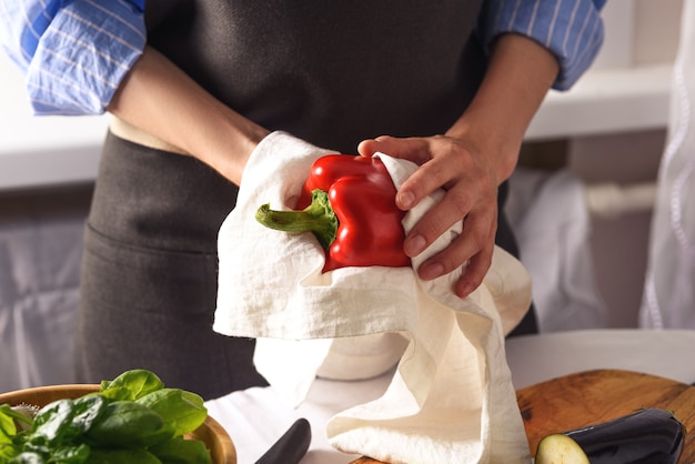 Closeup mujer limpia pimiento rojo con manos de toalla de cocina con verduras