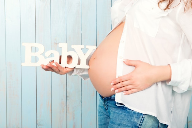 Foto closeup mujer sosteniendo un cartel de la palabra bebé en el fondo de una barriga embarazada