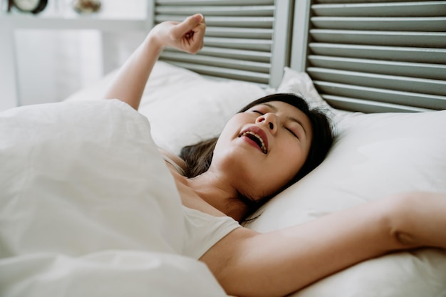 closeup mulher asiática deitada na cama de manhã está bocejando e esticando o corpo dela. senhora chinesa tendo uma boa noite de sono acordando de bom humor.