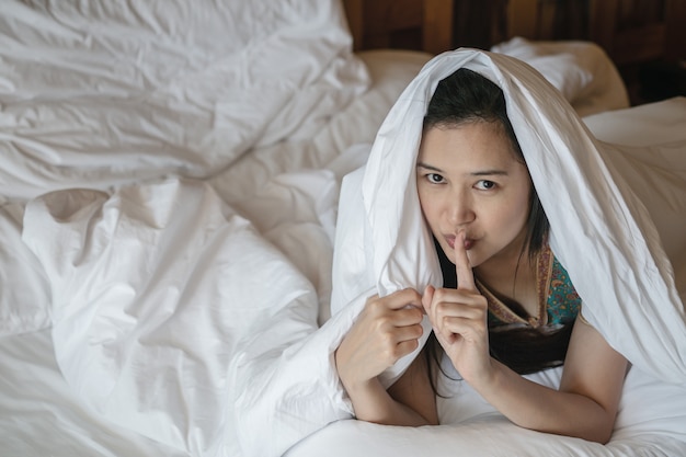 Closeup mulher asiática mentira na cama sob o cobertor e fazer um gesto para dizer o som suavemente