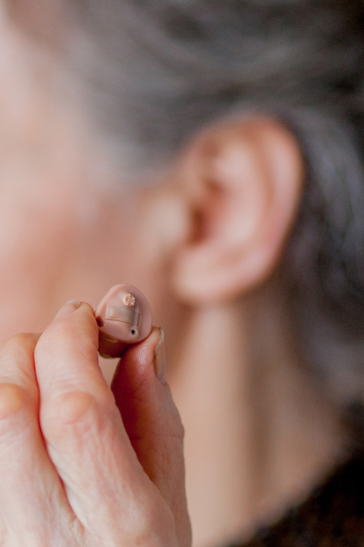 Foto closeup mulher idosa inserindo aparelho auditivo nos ouvidos
