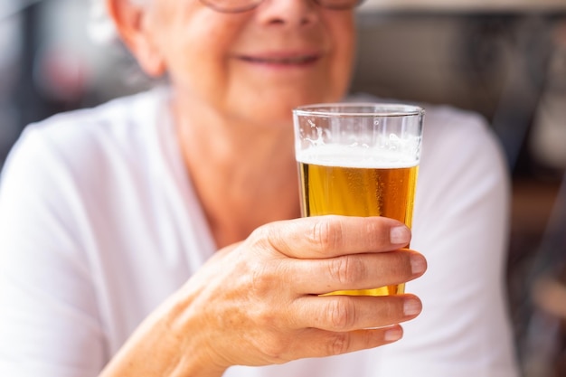 Closeup na mão de uma mulher sênior segurando um copo de cerveja loira gelada