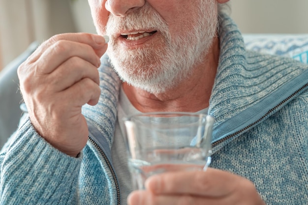 Closeup no homem barbudo sênior tomando uma pílula com um copo de cuidados de saúde de água e conceito de pessoas