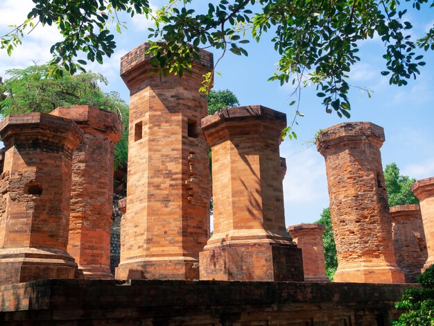 Foto closeup po nagar cham tower palos de piedra, antiguo templo en nha trang, vietnam en la sombra de árboles verdes con cielo azul nublado