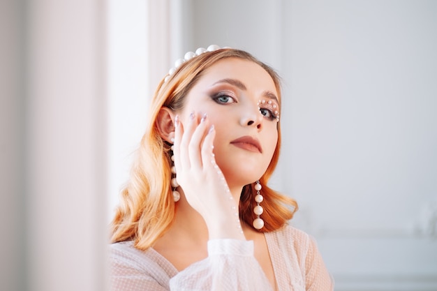 Closeup Portrait einer hübschen rothaarigen Frau mit Make-up aus Perlen auf ihrer Hand und Gesicht einer Perle...