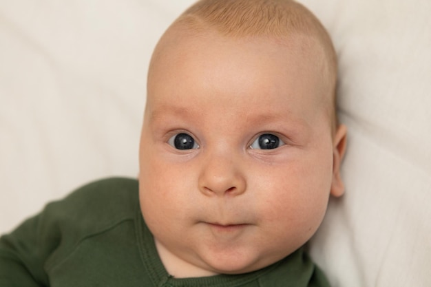 Closeup Portrait eines drei Monate alten Babys mit blauen Augen in Grün gekleidet