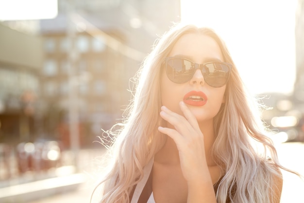 Closeup retrato de adorable modelo rubia con gafas, caminando en la ciudad en una tarde soleada. Espacio para texto