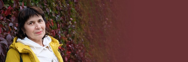 Closeup retrato de una anciana contra una pared de hojas de vid de otoño rojo