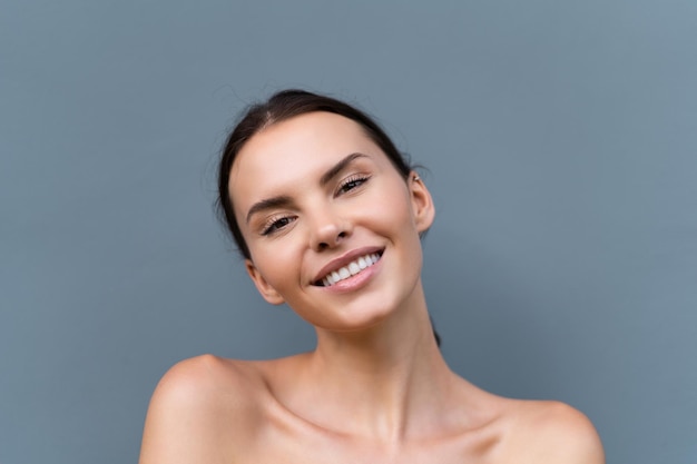 Closeup retrato de belleza de una mujer en topless con piel perfecta y maquillaje natural sobre fondo de pared azul claro reír y sonreír con dientes perfectos blancos como la nieve