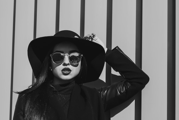 Foto closeup retrato callejero de mujer morena sensual lleva sombrero y gafas posando en la calle. tonificación en blanco y negro