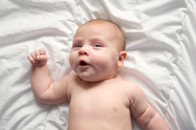 Closeup retrato de bebê recém-nascido no cobertor branco Foco suave O bebê está deitado bocejando Uma idade de duas semanas Menina acordando na cama em casa Nova vida e conceito de crescimento Pessoas reais