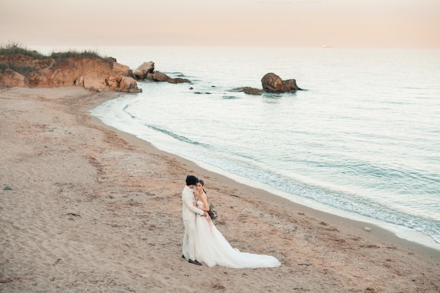 Foto closeup retrato de casamento jovem noiva e noivo com buquê posando na ilha exótica perto da água casal de lua de mel beijando no dia do casamento casal feliz apaixonado beijo de casamento casamento no mar