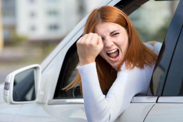 Closeup retrato de irritado descontente mulher agressiva com raiva, dirigindo um carro gritando com alguém com mão punho acima. conceito de expressão humana negativa