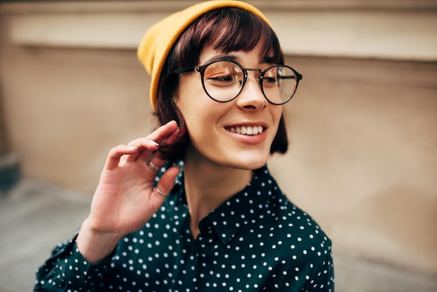 Closeup retrato de jovem feliz vestindo camisa verde com chapéu amarelo de pontos brancos e óculos transparentes Jovem estudante posando na rua da cidade