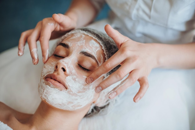 Foto closeup retrato de mãos de cosmetologistas aplicando máscara no rosto de clientes em salão de beleza natural de spa.