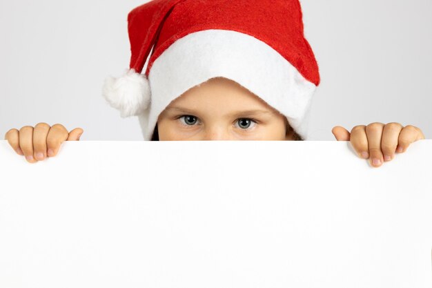 Closeup retrato de menina com chapéu de Papai Noel vermelho segurando cartaz em branco branco isolado no fundo branco wi ...