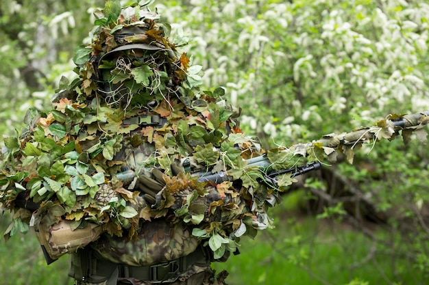 Closeup retrato de um atirador militar com roupas camufladas do exército verde e uma arma na mão no fundo de árvores floridas