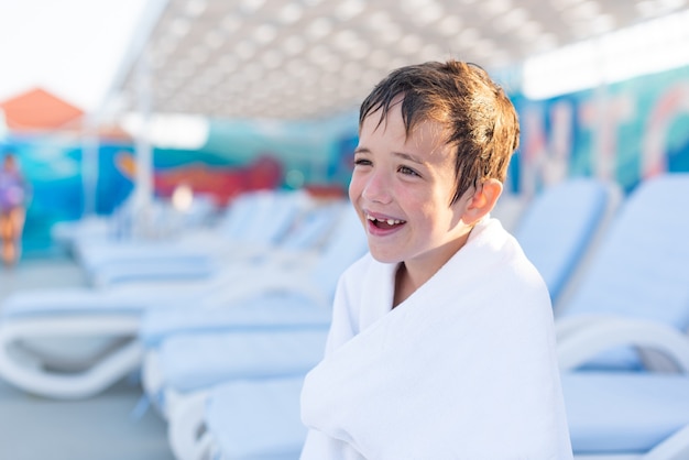 Closeup retrato de um menino sorridente enrolado em uma toalha depois de nadar na piscina externa