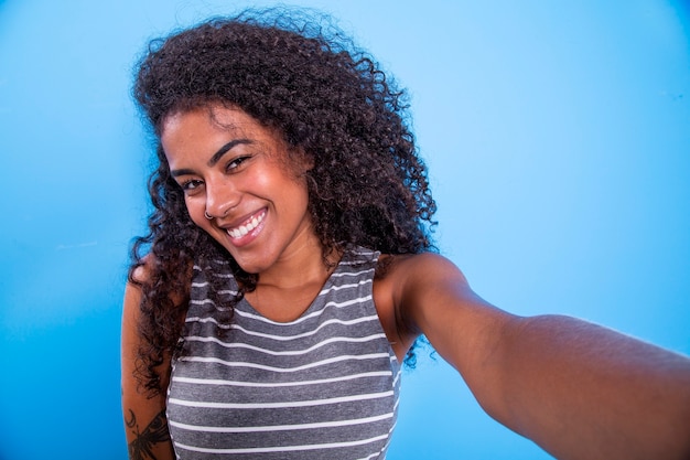 Closeup retrato de uma jovem e atraente mulher afro-brasileira sorridente, segurando um smartphone, tirando uma foto de selfie