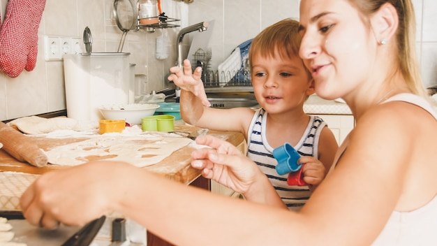Closeup retrato de uma jovem mãe com um filho pequeno segurando uma assadeira e fazendo biscoitos na cozinha
