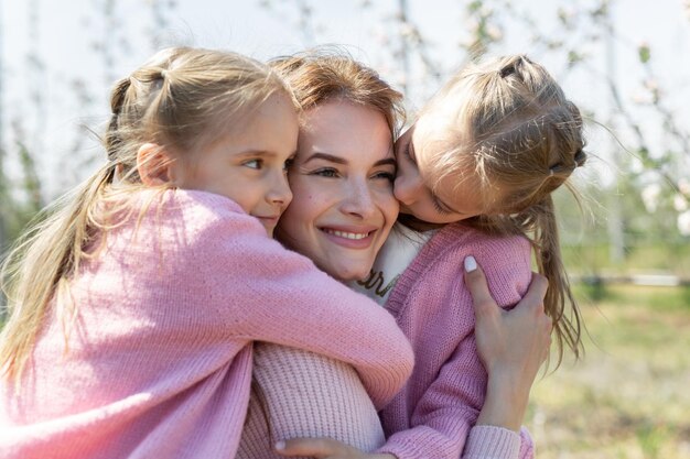 Closeup retrato de uma jovem mãe e suas filhas gêmeas se abraçando em um pomar de macieiras