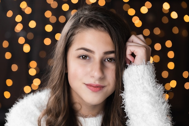 Closeup retrato de uma jovem muito bonita em fundo de luzes de bokeh de natal. retrato feminino atraente dentro de casa. retrato de uma mulher bonita com cordas quentes luzes festivas feriados