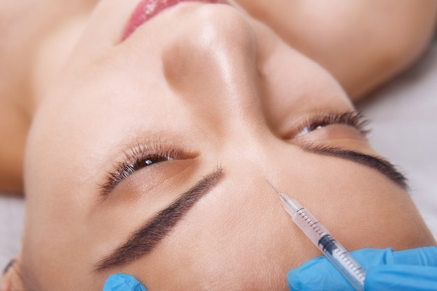 Closeup retrato de uma jovem mulher caucasiana, recebendo injeção plástica na testa. Pessoas, cosmetologia, cirurgia plástica e conceito de beleza.