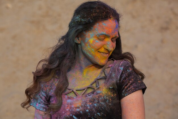 Closeup retrato de uma mulher morena alegre posando coberta com tinta seca Holi no deserto