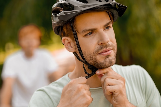 Closeup retrato de un deportista lindo barbudo serio ajustando las correas del casco debajo de la barbilla