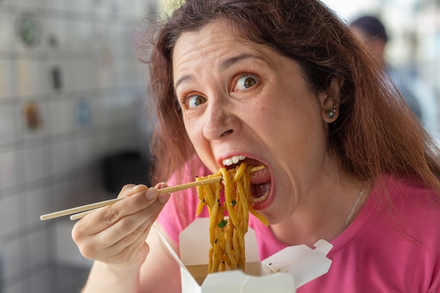 Foto closeup retrato de una divertida niña bonita loca comiendo fideos chinos con palillos de madera