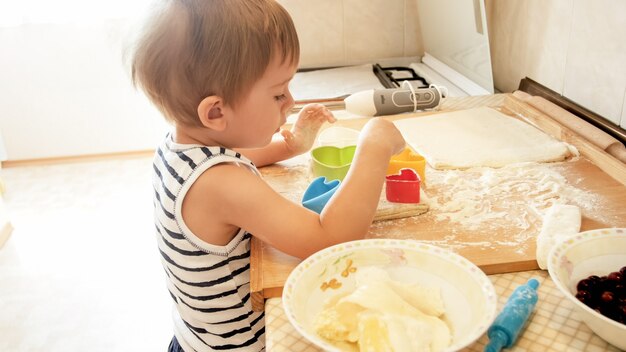 Closeup retrato do menino fofo da criança de 3 anos de pé na cozinha e cozinhar massa. Criança assando e fazendo café da manhã