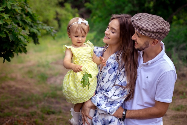 Closeup retrato de familia joven hermosa que lleva a una pequeña niña con estilo en el parque verde en un cálido día de verano