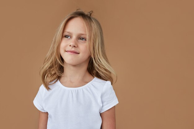 Closeup retrato frontal de adorable niña con cabello rubio ondulado, vestida con ropa blanca