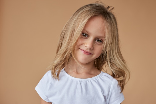 Closeup retrato frontal de niña bonita con cabello rubio ondulado, vestida con ropa blanca