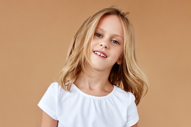 Closeup retrato frontal de niña bonita con cabello rubio ondulado, vestida con ropa blanca