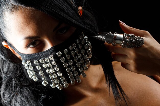 Closeup retrato de hermosa mujer morena con arte corporal facial ocultando la mitad de su cara con máscara