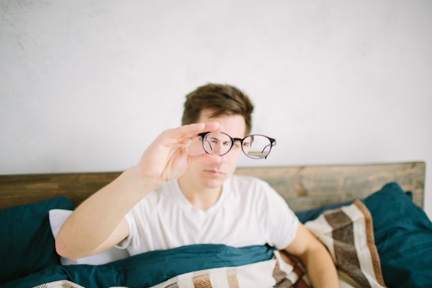 Closeup retrato de hombre joven con gafas. tiene problemas de visión y está entrecerrando los ojos un poco. chico guapo está sosteniendo sus anteojos justo en frente de la cámara con una mano