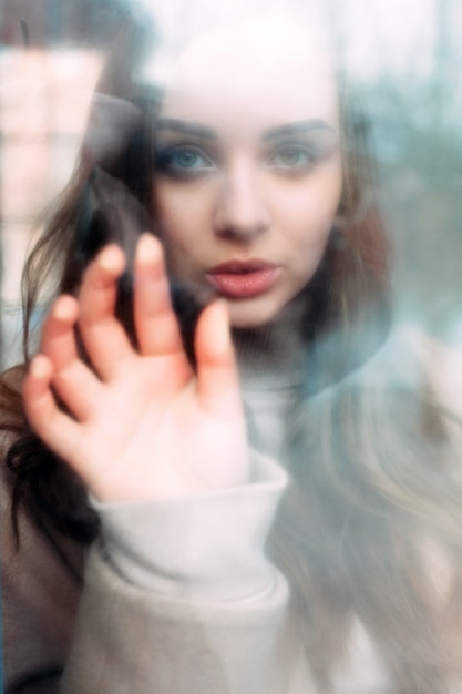 Closeup retrato de invierno de joven morena sensual mirando triste a través de la ventana tocando la ventana